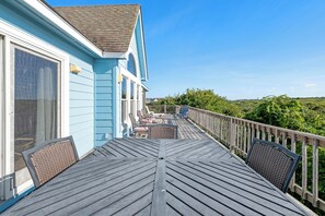 A wooden deck with outdoor furniture, a railing, and a view of greenery.