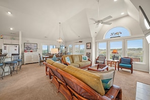 A spacious living area with a high ceiling, a dining table, and a large window offering a view of the outdoors. - Spacious water-view 7BR - private pool & hot tub (Corolla)