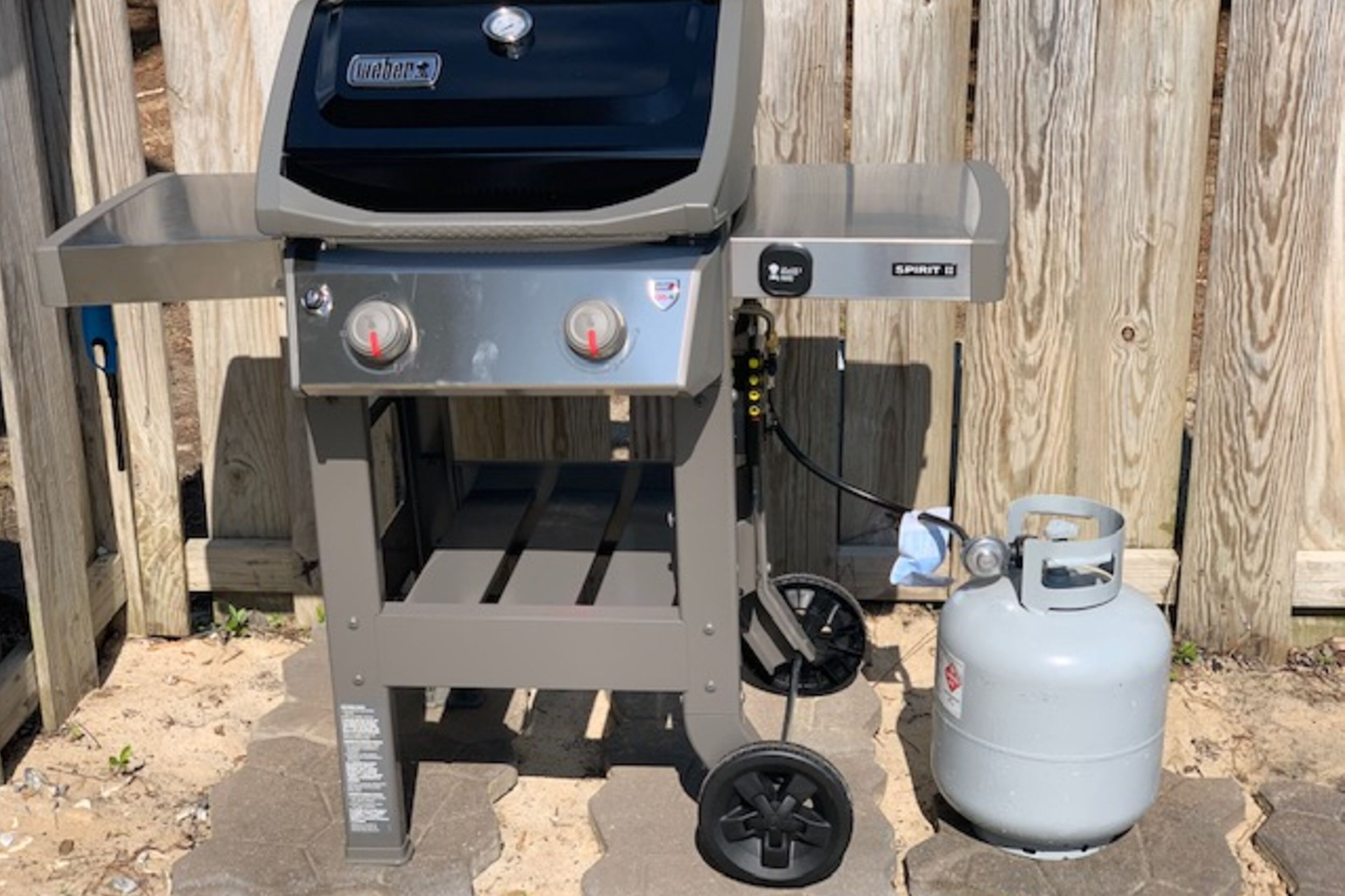 A portable gas grill with two control knobs, a propane tank, and a metal frame.