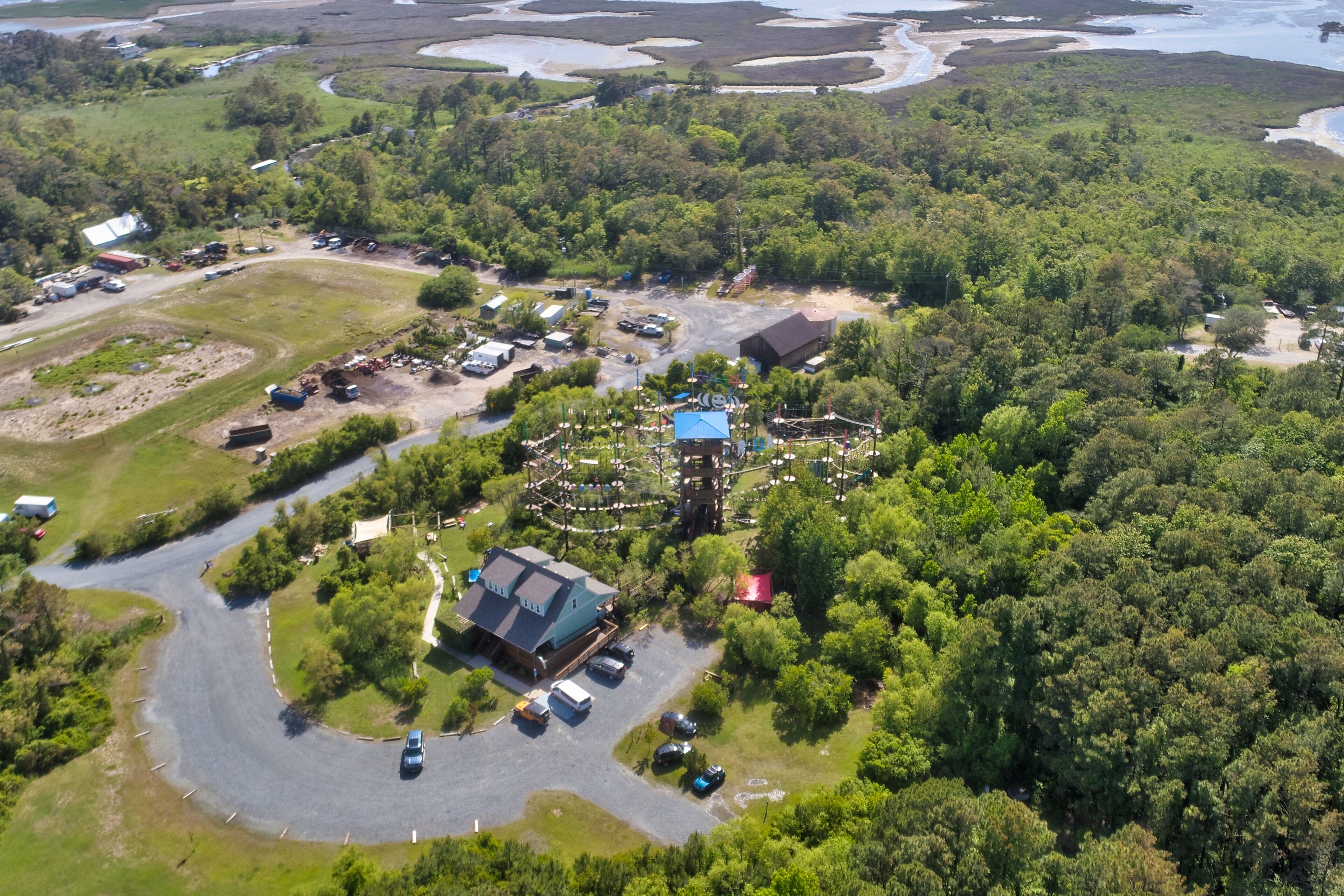 An aerial view of a property with a large building, parking area, and surrounding greenery.