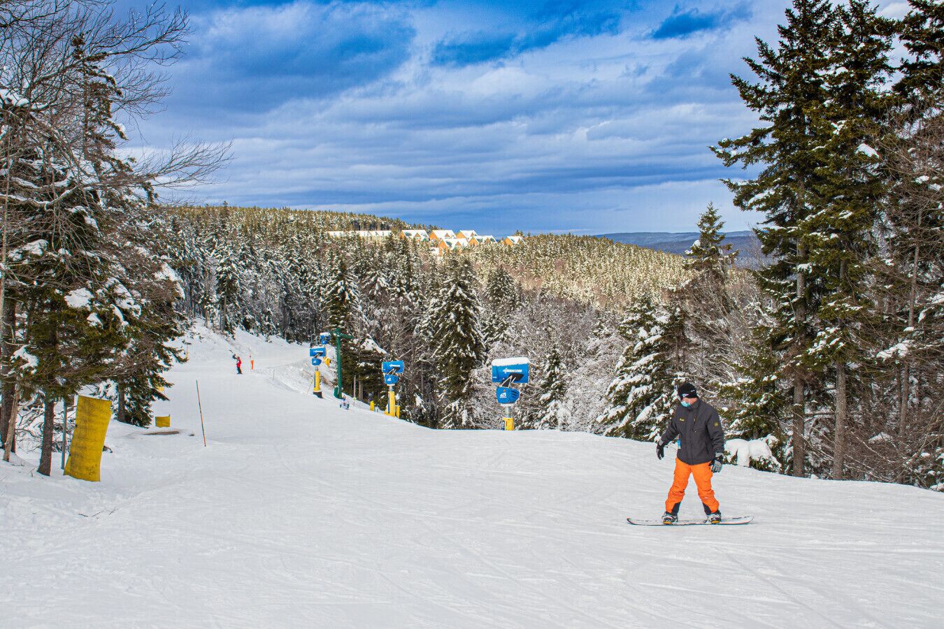 Una pista de esquí nevada con un esquiador que viste pantalones naranja y una chaqueta negra.
