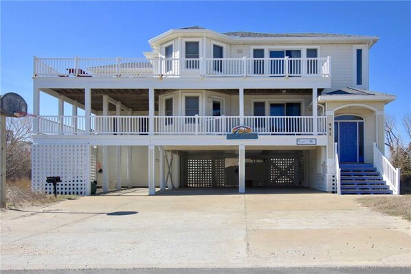 A two-story building with a balcony on the upper floor, a garage entrance, and a blue door. - 5BR | Private Pool | Hot Tub | Balcony | W/D (Corolla)