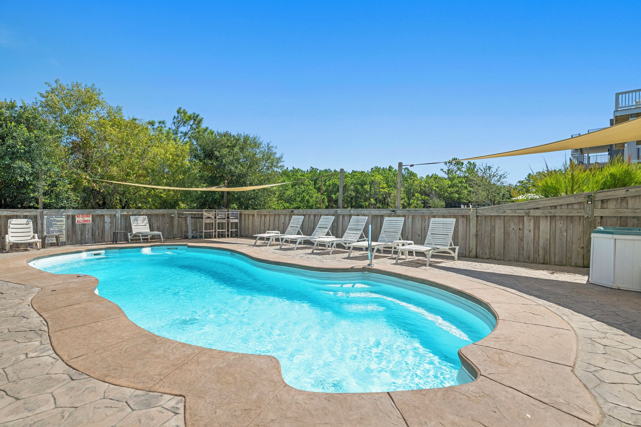 A swimming pool with lounge chairs and a wooden fence.