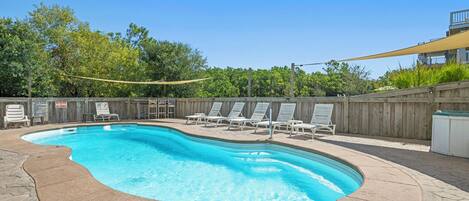 A swimming pool with lounge chairs and a wooden fence.