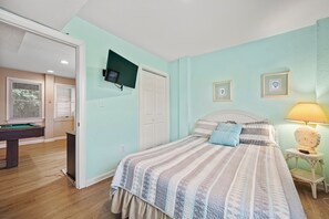A bedroom with a bed, a television mounted on the wall, a lamp, and a billiards table.
