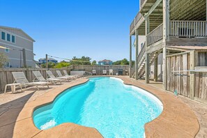 A swimming pool with a wooden deck, lounge chairs, and a wooden deck structure.