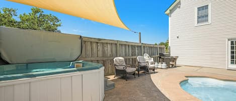 Un patio trasero con jacuzzi, mobiliario exterior y una piscina.