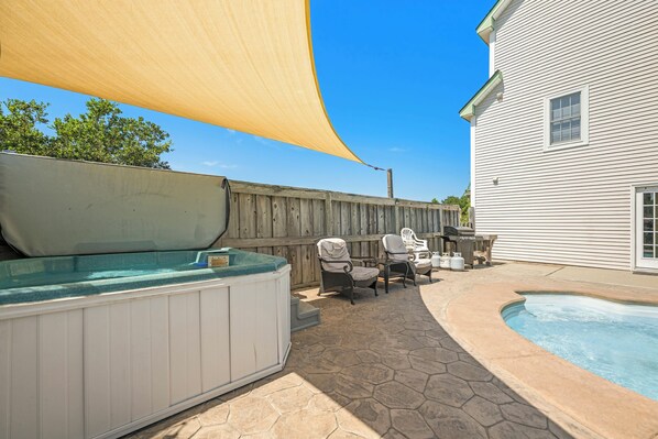 A backyard with a hot tub, outdoor seating, and a swimming pool.