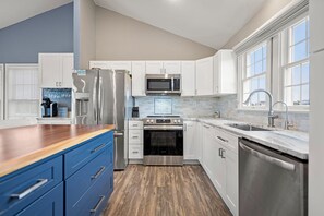 A modern kitchen with stainless steel appliances, white cabinetry, and a wooden countertop.