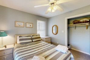 A bedroom with a bed, a nightstand, a lamp, a ceiling fan, a window with blinds, a mirror, and a closet with shelves. - 7BR Dog Friendly | Pool | Hot Tub | Deck | W/D (Corolla)