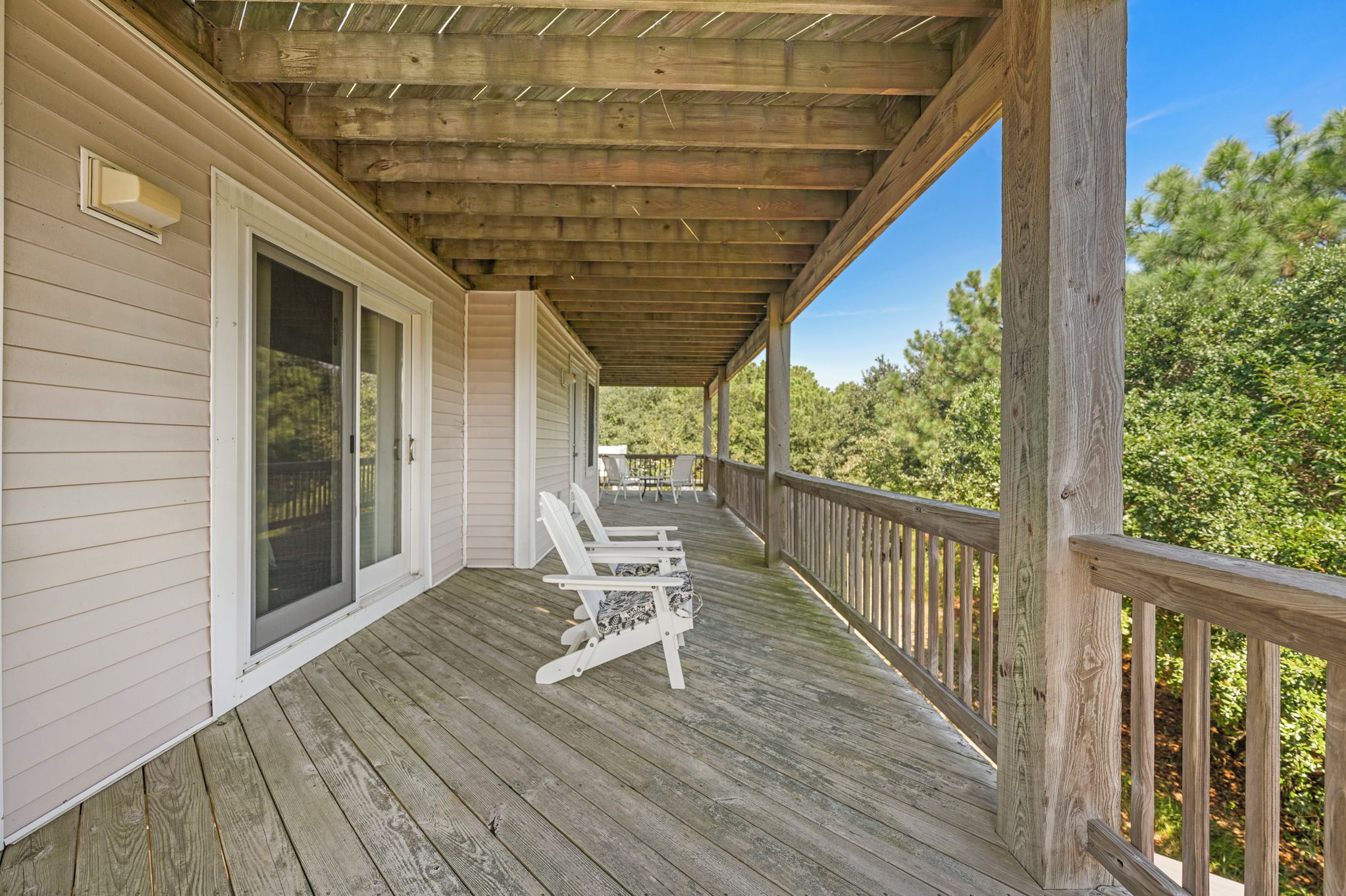 A wooden deck with a covered porch, a sliding glass door, and a view of trees.