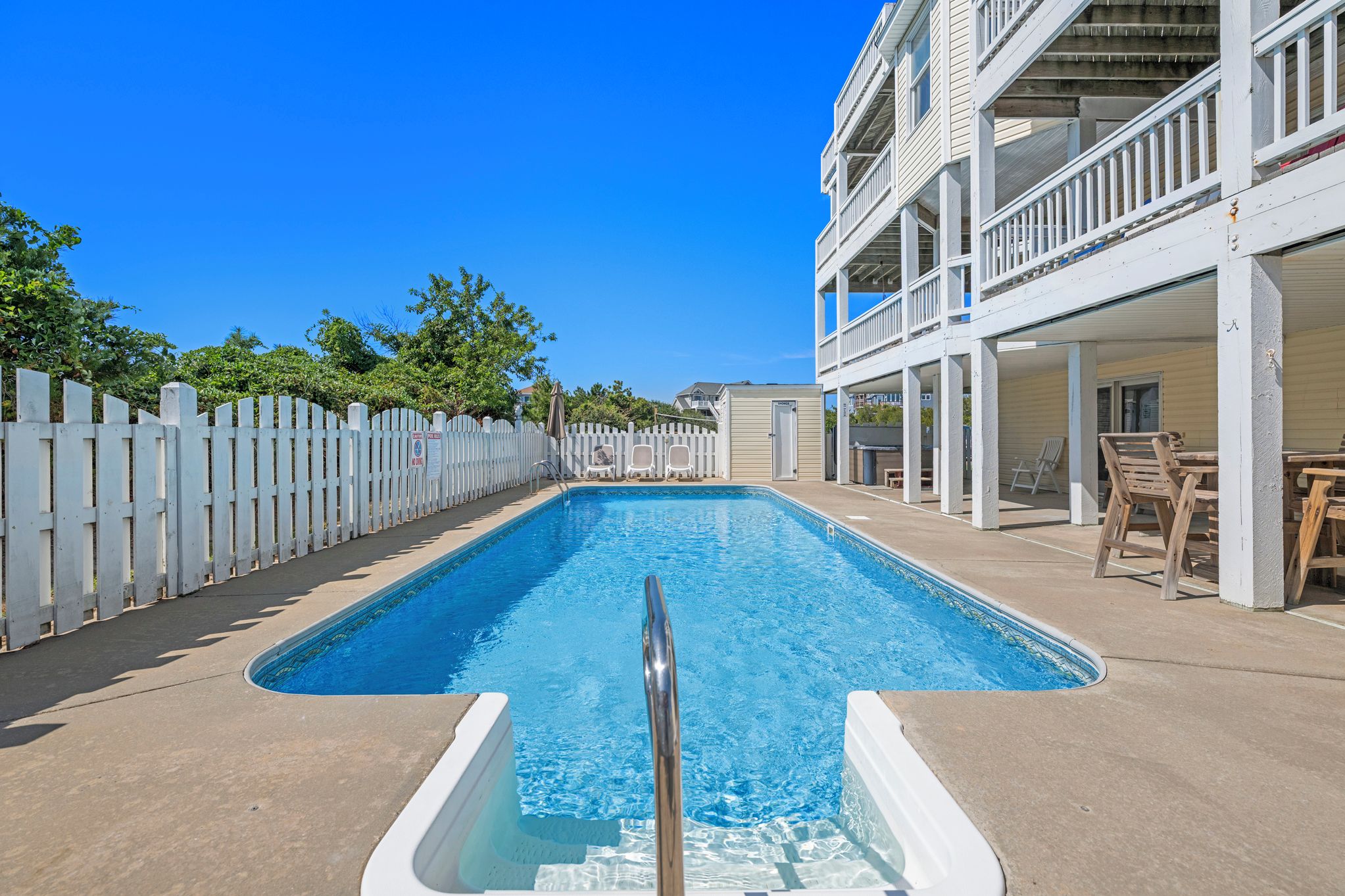 A swimming pool with a white fence, lounge chairs, and a building with balconies.