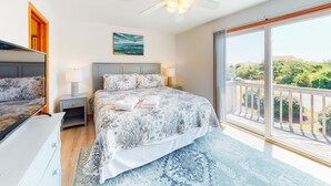 A bedroom with a bed, nightstands, a ceiling fan, a painting, and a balcony with a view. - 2BR | Pool | Deck | Tennis | W/D (Duck)