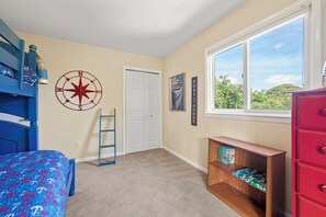 A bedroom with a bunk bed, a desk with a chair, a bookshelf, a window with a view, and a door. - Walk to Beach 5BR Waterview Dog Friendly | Pool (Duck)
