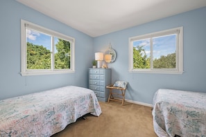 A bedroom with two beds, a dresser, a chair, and a window with a view of trees.