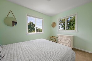 A bedroom with a bed, dresser, two windows, and a wall-mounted mirror.