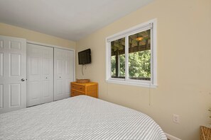 A bedroom with a bed, a dresser, a television, and a window with a view of trees.