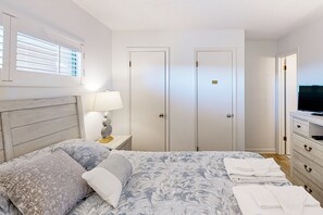 A bedroom with a bed, a nightstand with a lamp, a dresser, and a television. - 1BR Oceanfront condo with a pool and tennis court (Duck)