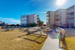 A modern apartment complex with multiple balconies, a wooden deck, and picnic tables. - 1BR Oceanfront condo with a pool and tennis court (Duck)