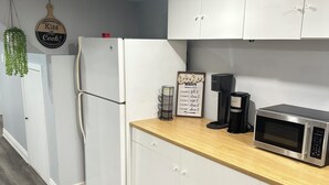 A modern kitchen with white cabinets, a wooden countertop, a stainless steel refrigerator, a microwave, a coffee maker, and a kitchen rules sign. - Soft landing spot | Relaxed basement hideout (Ajax)