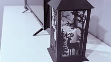 A black lantern with a deer silhouette and trees on a white surface.