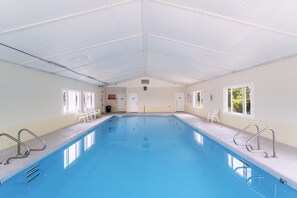 An indoor swimming pool with clear blue water, white walls, and a high ceiling.