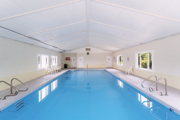 An indoor swimming pool with clear blue water, white walls, and a high ceiling.