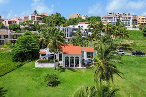 A large, multi-story building with a red-tiled roof, surrounded by lush greenery and palm trees.