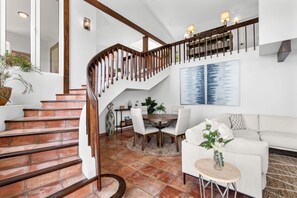 A staircase with wooden railings, a dining area with a round table and chairs, and a white sofa.