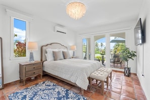 Une chambre à coucher comprenant un lit, des tables de chevet, un banc, un lustre et un téléviseur.