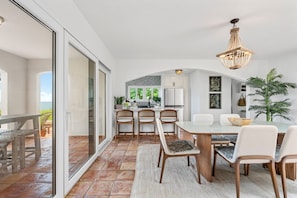 A modern kitchen with white cabinets, a dining area with a glass table, and a large sliding glass door leading to an outdoor patio.