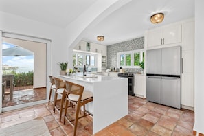 A modern kitchen with a central island, white cabinetry, and a view to the outside.