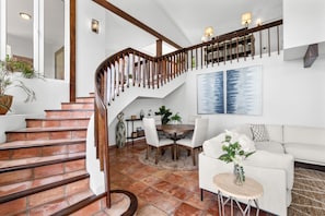 A staircase with wooden railings, a dining area with a round table and chairs, and a white sofa.