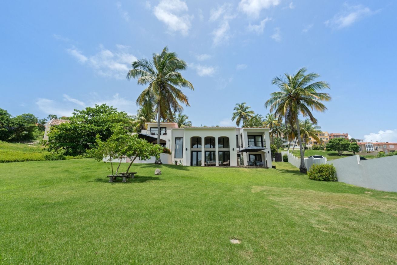 A modern building with a large lawn, palm trees, and a clear sky.