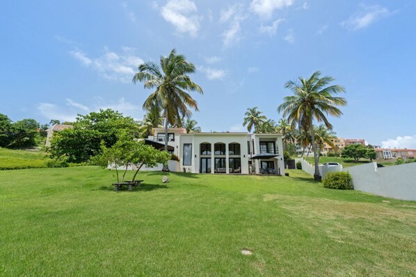 A modern building with a large lawn, palm trees, and a clear sky.