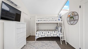 Un dormitorio con una cama litera, televisión, cómoda, alfombra estampada y un adorno circular en la pared.