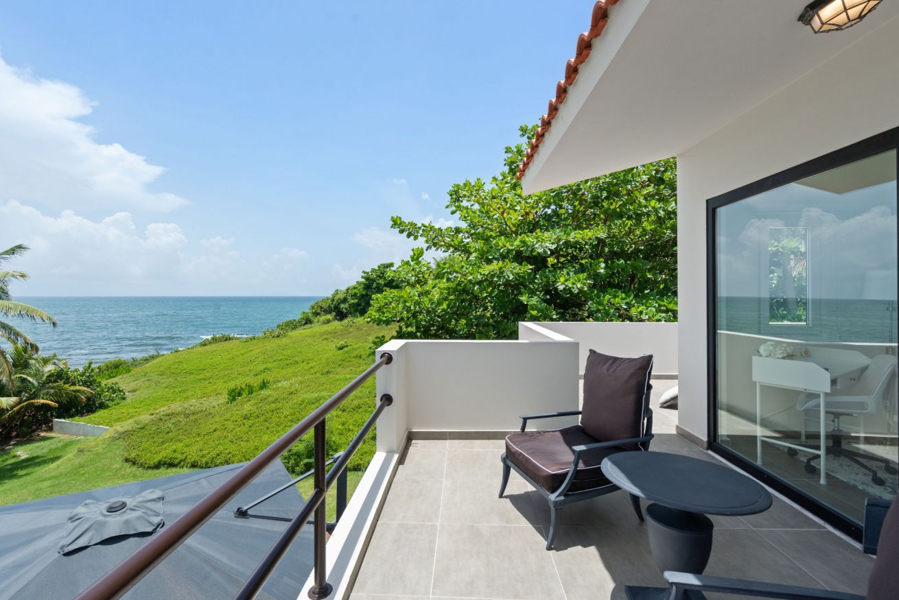A balcony with a view of the ocean, a chair, a table, and a glass door.
