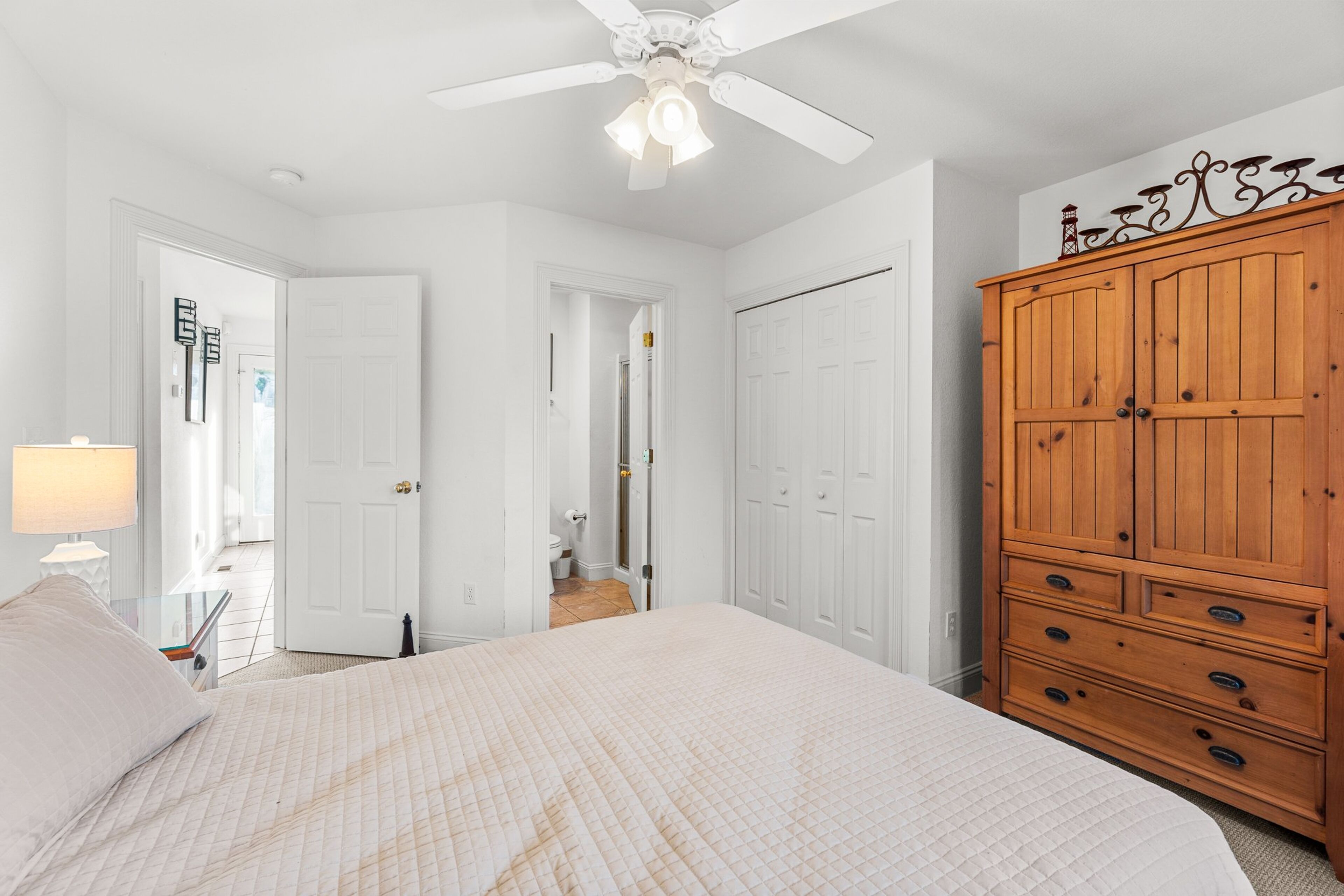 A bedroom with a bed, a wardrobe, a ceiling fan, and a door leading to a bathroom.