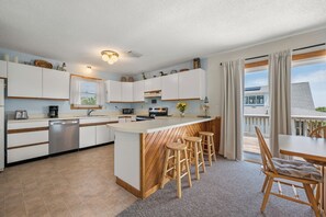A modern kitchen with white cabinets, a central island, wooden stools, and a dining table with chairs.