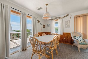 A dining area with a wooden table and chairs, a hanging light fixture, and a view of the outdoors. - Oceanside 3BR, walk to beach & boardwalk (Duck)