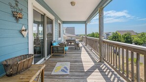 Un porche cubierto con una terraza de madera, mobiliario exterior y vistas al océano.