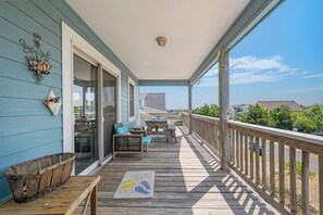 A covered porch with a wooden deck, outdoor furniture, and a view of the ocean. - Oceanside 3BR, walk to beach & boardwalk (Duck)