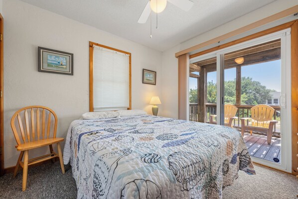 A bedroom with a bed, a chair, a window with blinds, and a view of the outdoors.