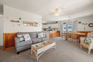 A living room with a grey sofa, a glass coffee table, and a wooden dining table with chairs.