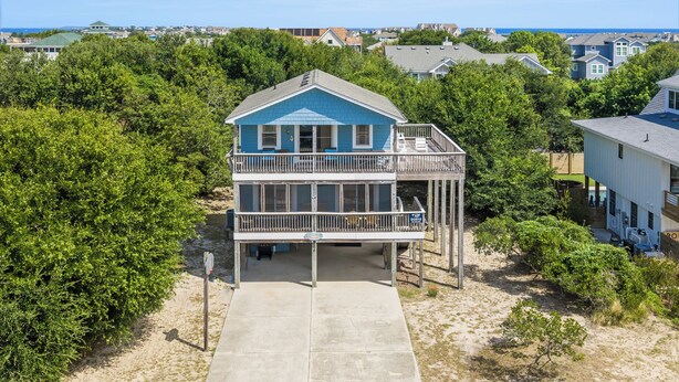 Casa frente al mar de dos pisos con balcón, rodeada de vegetación y otras edificaciones residenciales.
