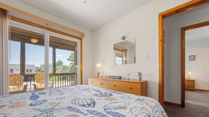 Un dormitorio con cama, cómoda, espejo y un balcón con sillas.