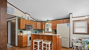 A compact kitchen with wooden cabinets, a microwave, a refrigerator, and a small island with stools.