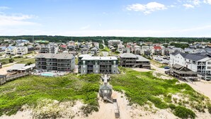A coastal town with a prominent building featuring multiple balconies, a beach area with a wooden walkway, and a clear view of the surrounding residential area. - Serene 2BR Oceanfront 3rd-Floor | Balcony | Pool (Kill Devil Hills)