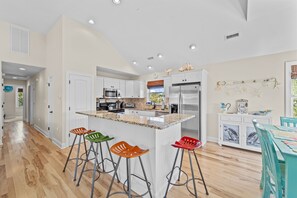 A modern kitchen with white cabinets, a central island with stools, stainless steel appliances, and a decorative wall with sea-themed items.