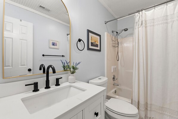 A bathroom with a white sink, black faucet, a framed picture, a toilet, and a shower with a curtain.